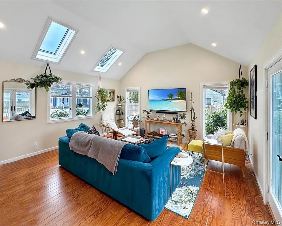 Living room with a skylight, lofted ceiling, hardwood / wood-style floors, and recessed lighting Living room with a skylight, lofted ceiling, hardwood / wood-style floors, and recessed lighting
