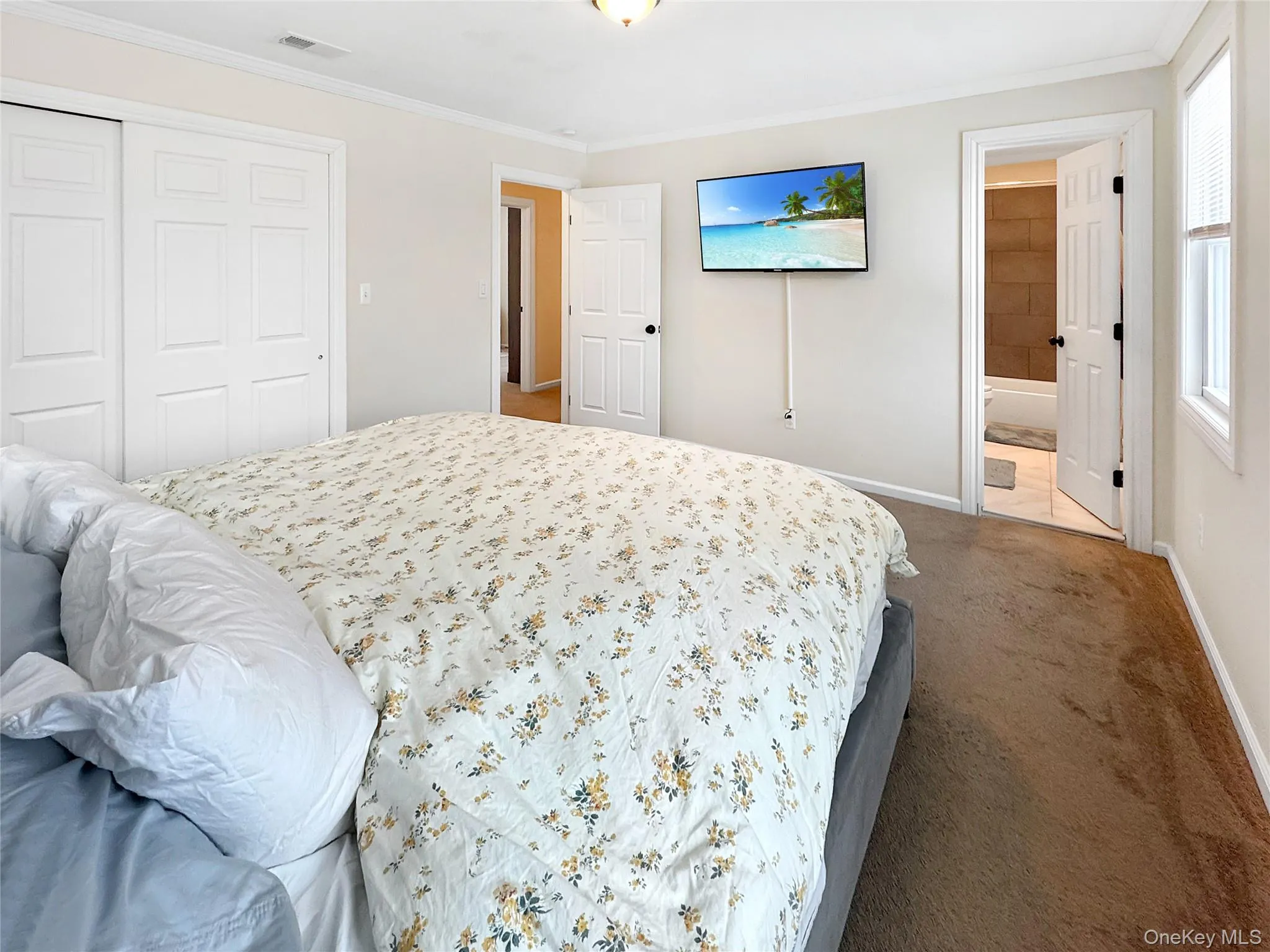 Bedroom featuring ornamental molding, dark colored carpet, a closet, and connected bathroom Bedroom featuring ornamental molding, dark colored carpet, a closet, and connected bathroom