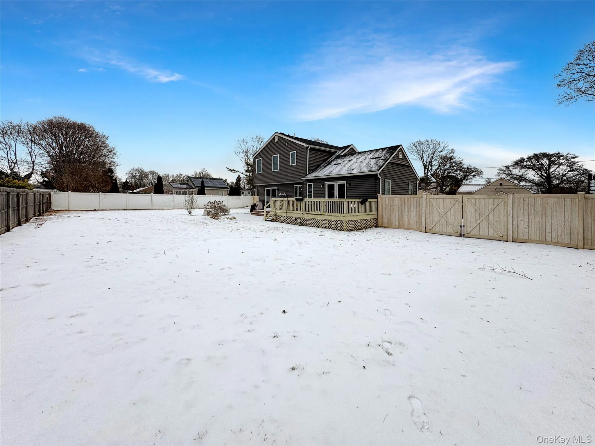 Snow covered rear of property featuring a fenced backyard, a wooden deck, and a gate Snow covered rear of property featuring a fenced backyard, a wooden deck, and a gate