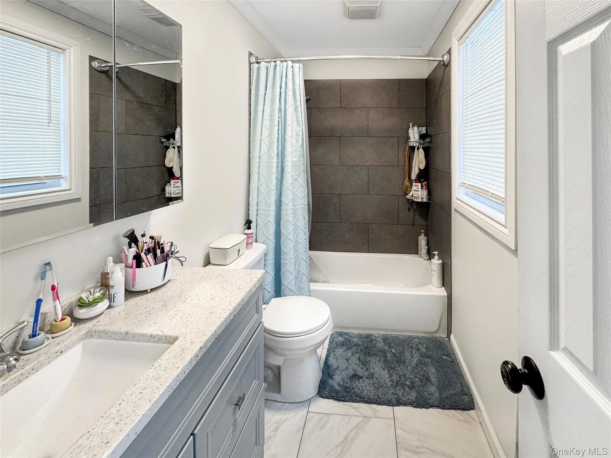 Full bath with healthy amount of natural light, shower / bath combo, vanity, and ornamental molding Full bath with healthy amount of natural light, shower / bath combo, vanity, and ornamental molding