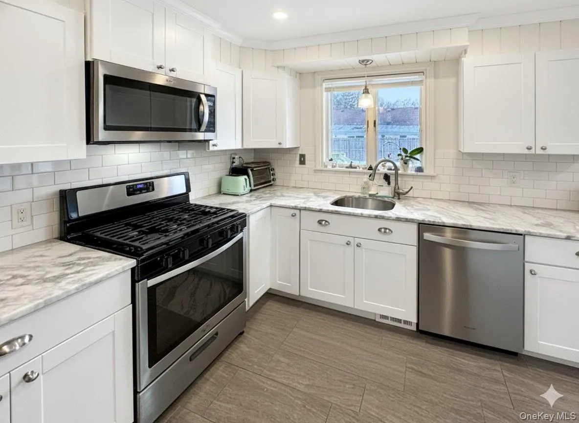 Kitchen featuring stainless steel appliances, light stone countertops, white cabinetry, tasteful backsplash, and crown molding Kitchen featuring stainless steel appliances, light stone countertops, white cabinetry, tasteful backsplash, and crown molding