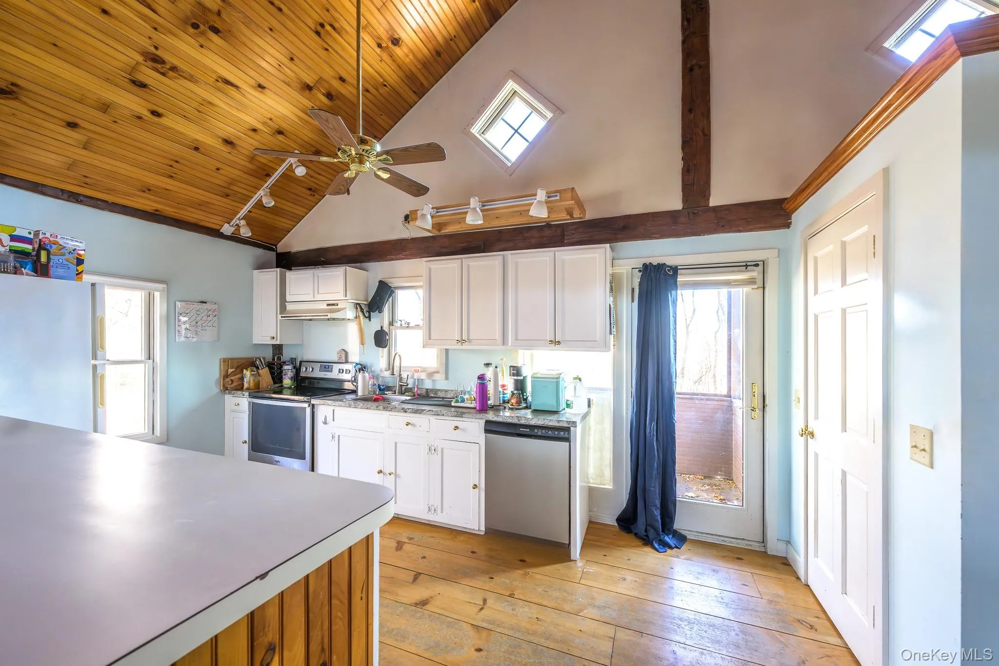 Kitchen with appliances with stainless steel finishes, white cabinets, ceiling fan, plenty of natural light, and high vaulted ceiling Kitchen with appliances with stainless steel finishes, white cabinets, ceiling fan, plenty of natural light, and high vaulted ceiling