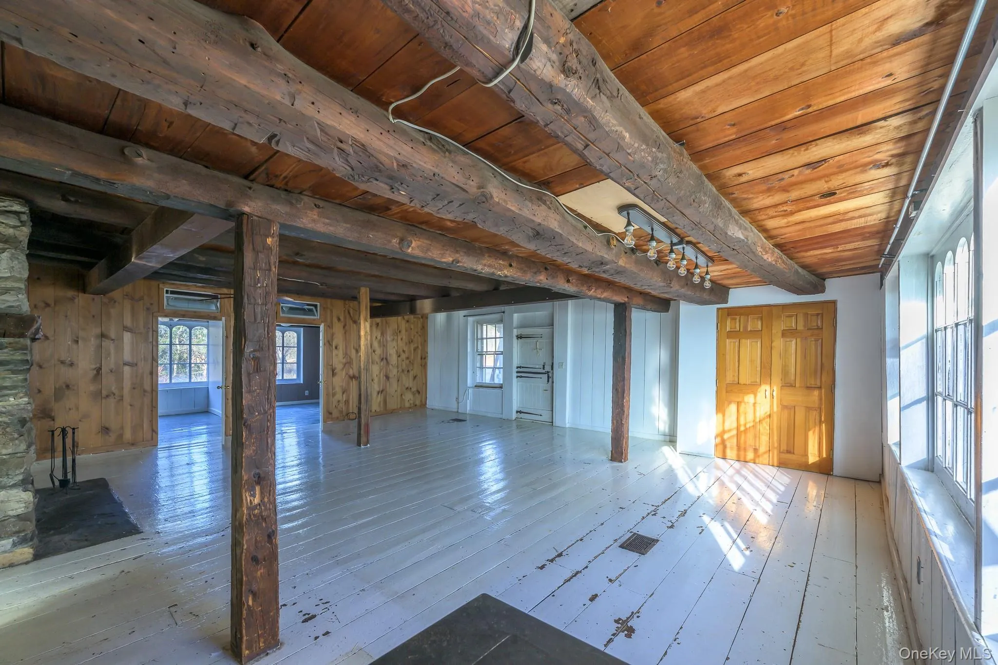 Unfurnished living room featuring a wooden ceiling with exposed beams, healthy amount of natural light, hardwood / wood-style flooring, and wood walls Unfurnished living room featuring a wooden ceiling with exposed beams, healthy amount of natural light, hardwood / wood-style flooring, and wood walls