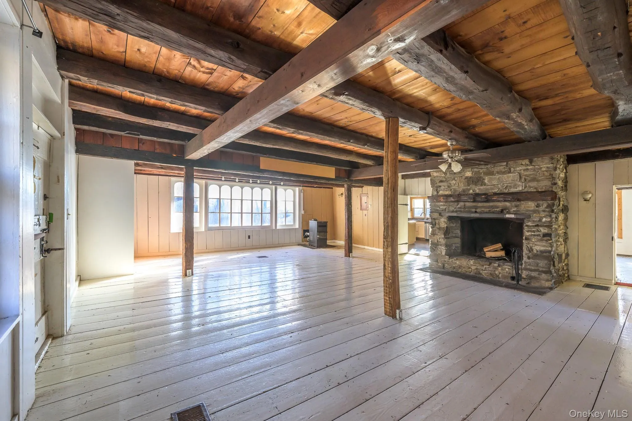 Unfurnished living room featuring wood walls, a fireplace, a ceiling fan, light wood-style floors, and a wooden ceiling with exposed beams Unfurnished living room featuring wood walls, a fireplace, a ceiling fan, light wood-style floors, and a wooden ceiling with exposed beams