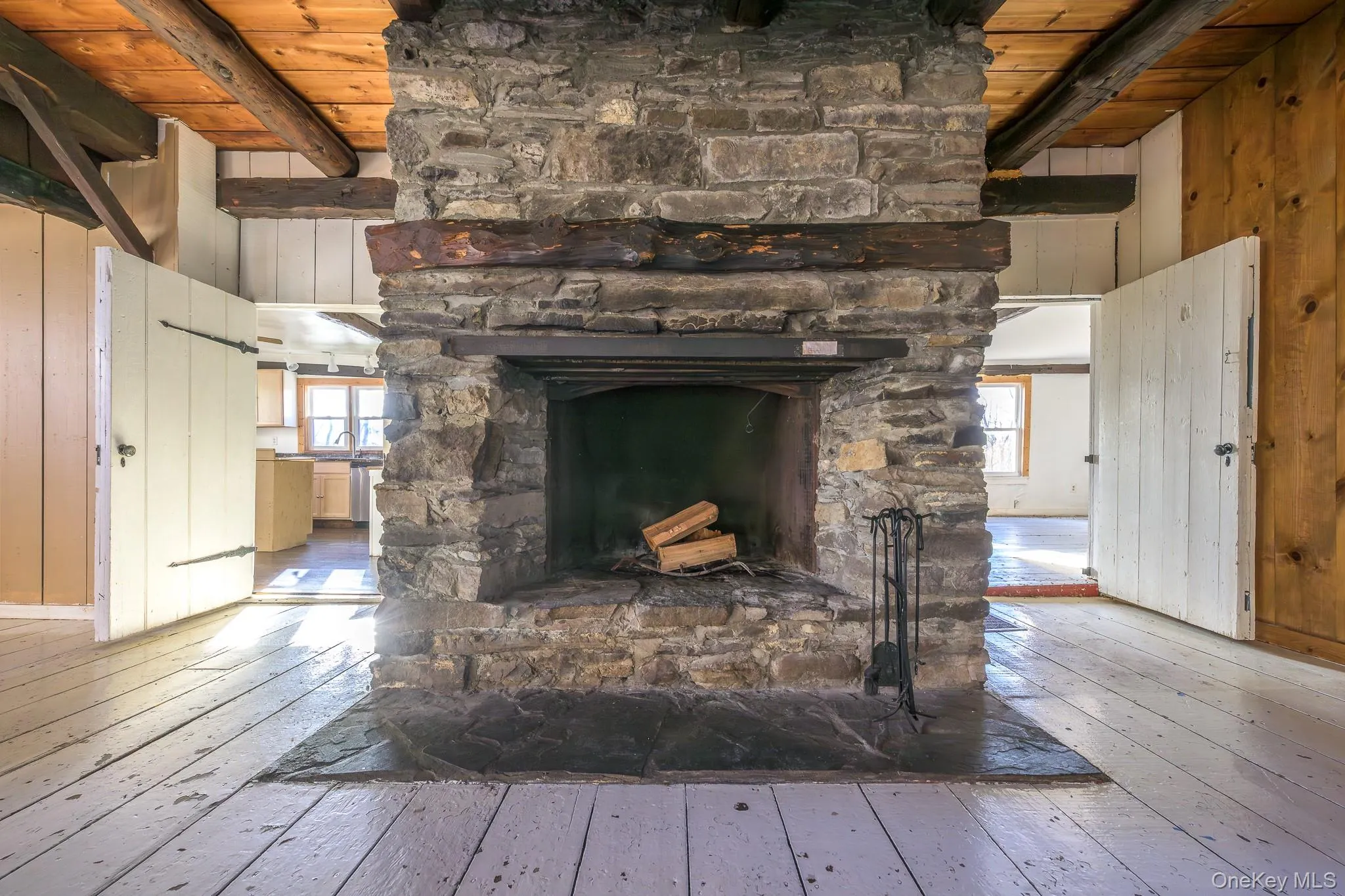 Detailed view of a wood ceiling with exposed beams, wooden walls, wood finished floors, and a stone fireplace Detailed view of a wood ceiling with exposed beams, wooden walls, wood finished floors, and a stone fireplace