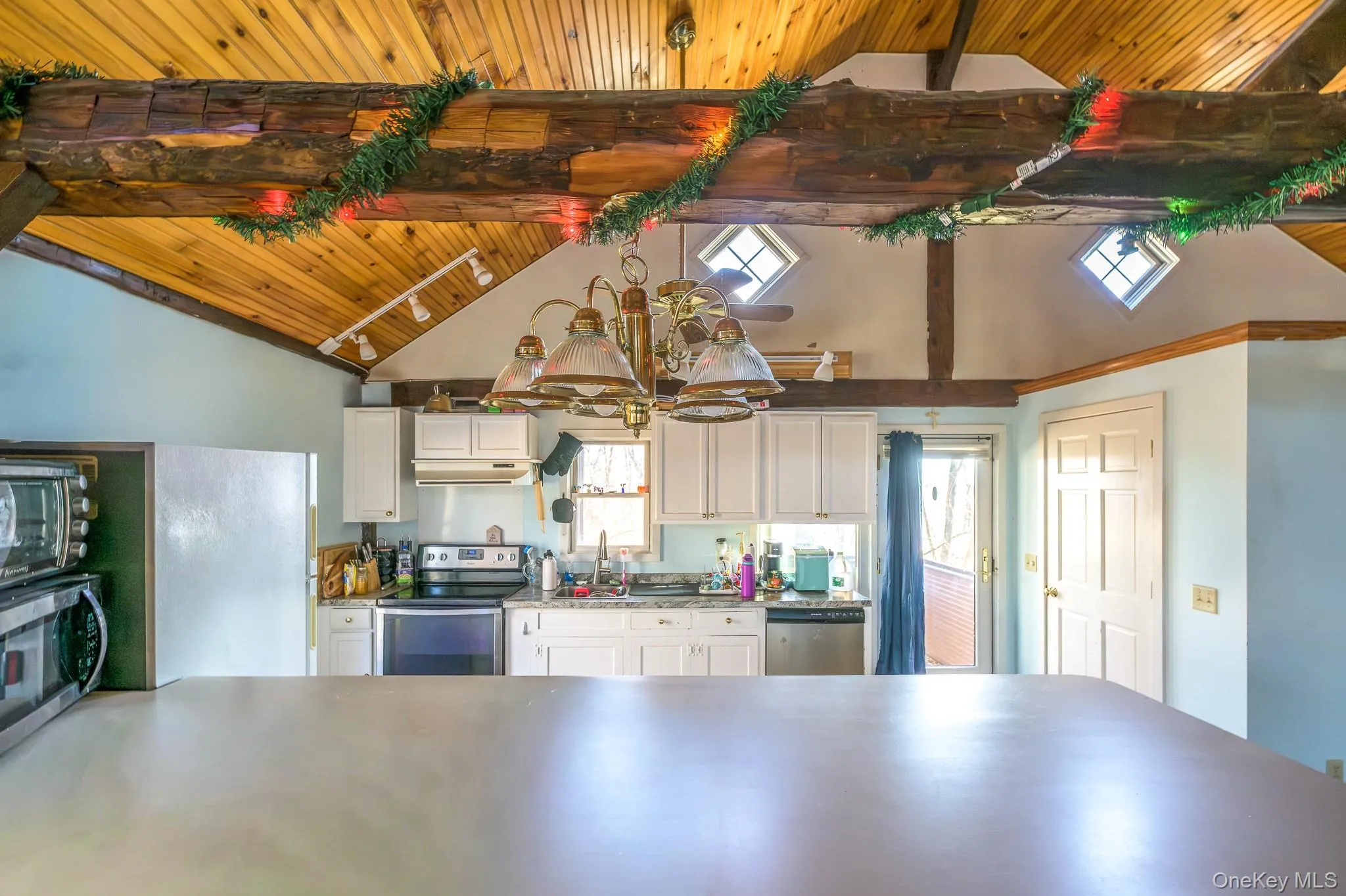 Kitchen featuring appliances with stainless steel finishes, white cabinets, a wood ceiling with exposed beams, high vaulted ceiling, and pendant lighting Kitchen featuring appliances with stainless steel finishes, white cabinets, a wood ceiling with exposed beams, high vaulted ceiling, and pendant lighting