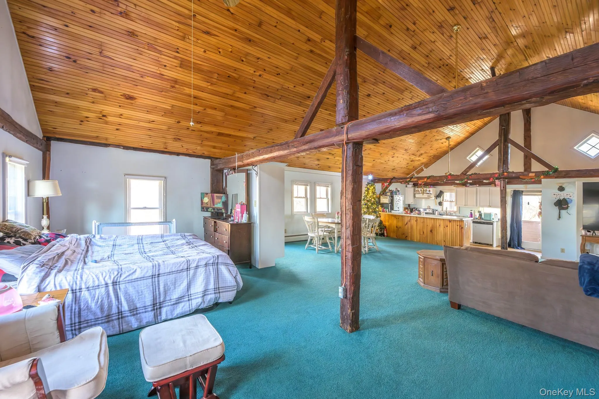 Carpeted bedroom with a wooden ceiling with exposed beams, high vaulted ceiling, and a baseboard heating unit Carpeted bedroom with a wooden ceiling with exposed beams, high vaulted ceiling, and a baseboard heating unit