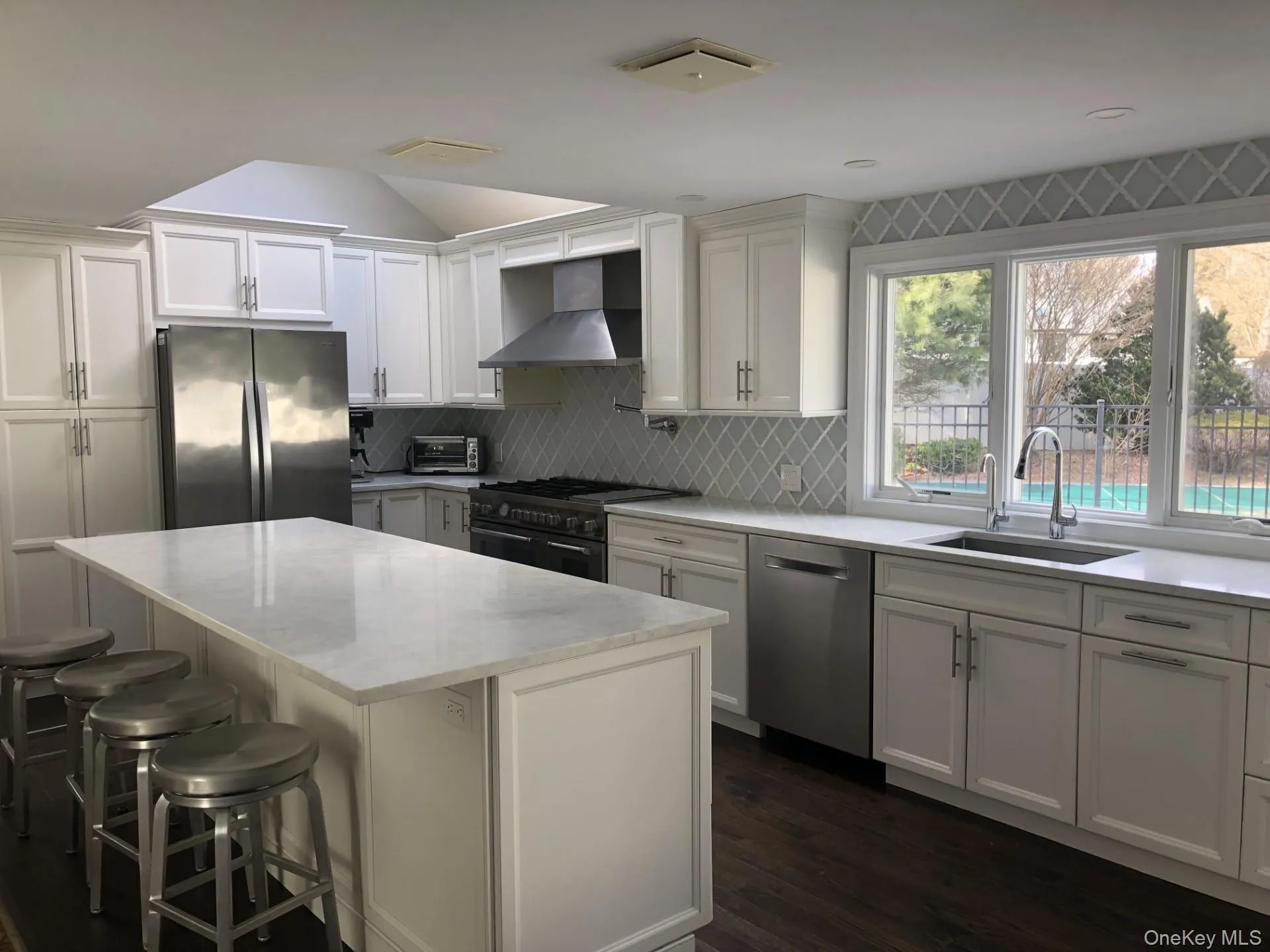 Kitchen featuring a center island, wall chimney exhaust hood, a sink, stainless steel appliances, and backsplash Kitchen featuring a center island, wall chimney exhaust hood, a sink, stainless steel appliances, and backsplash