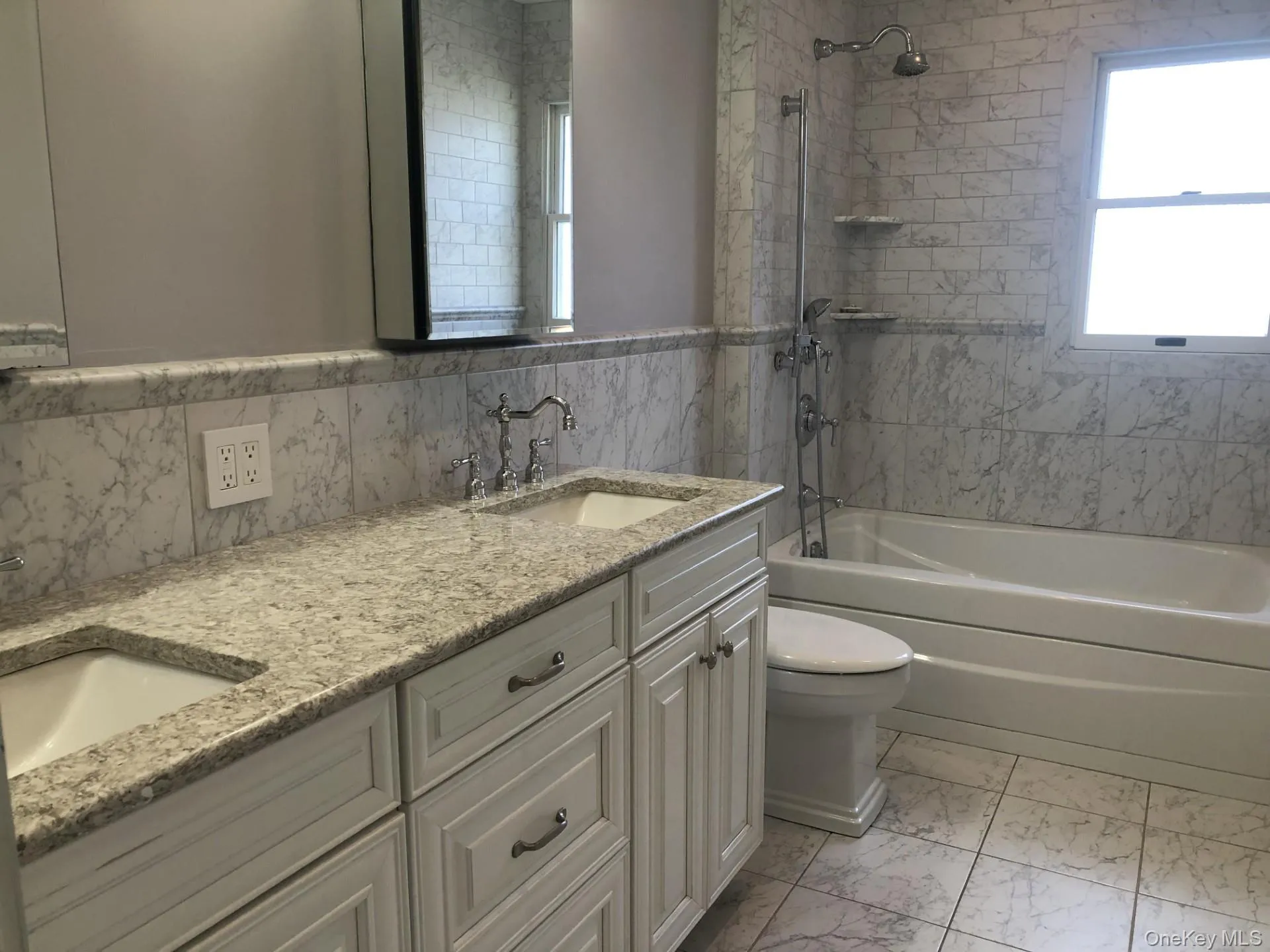 Bathroom featuring double vanity, bathing tub / shower combination, toilet, marble finish floor, and a sink Bathroom featuring double vanity, bathing tub / shower combination, toilet, marble finish floor, and a sink