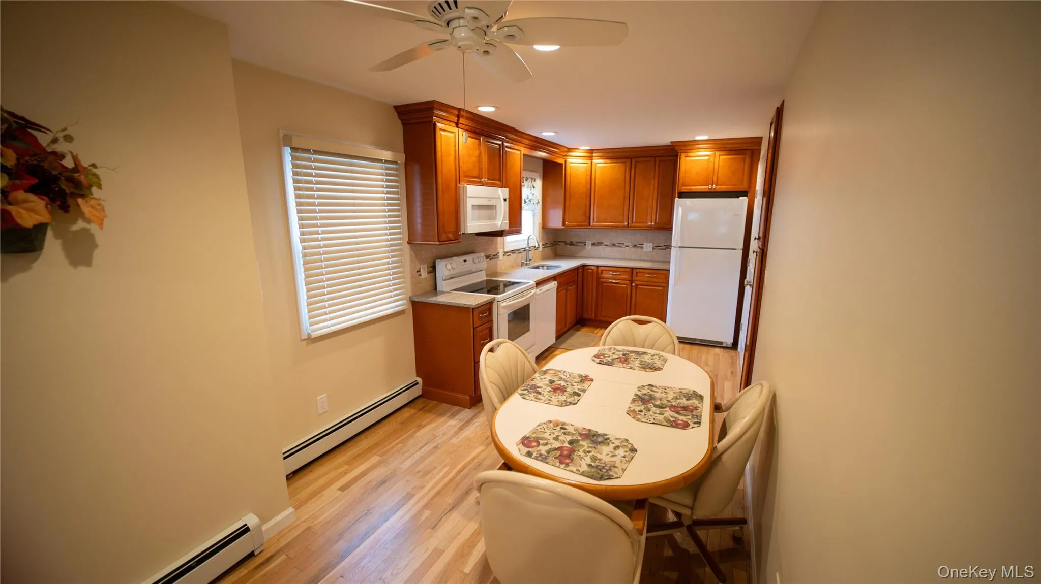 Kitchen featuring white appliances, brown cabinets, a baseboard heating unit, a ceiling fan, and recessed lighting Kitchen featuring white appliances, brown cabinets, a baseboard heating unit, a ceiling fan, and recessed lighting