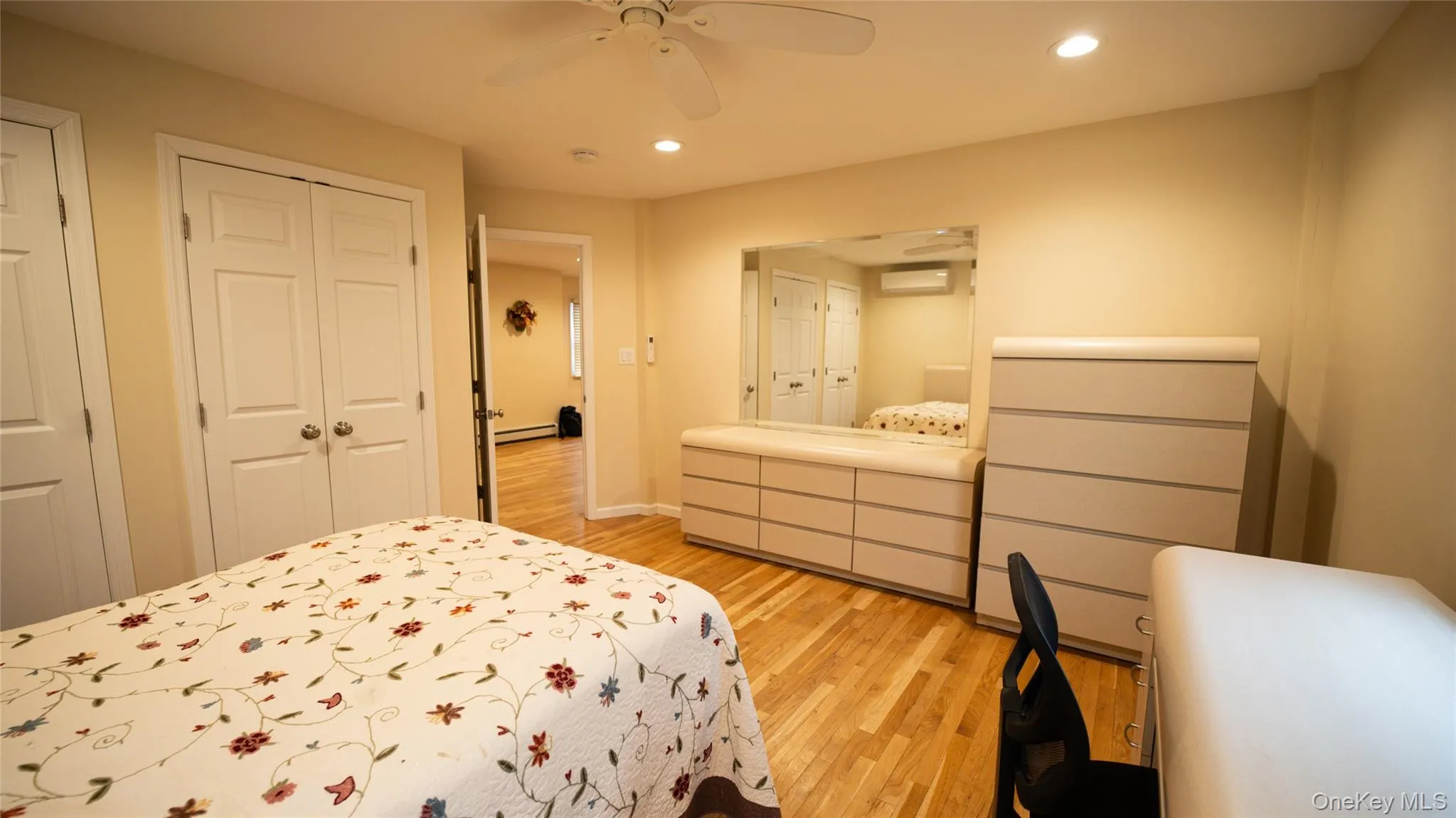 Bedroom featuring light wood-style floors, recessed lighting, a ceiling fan, two closets, and an AC wall unit Bedroom featuring light wood-style floors, recessed lighting, a ceiling fan, two closets, and an AC wall unit