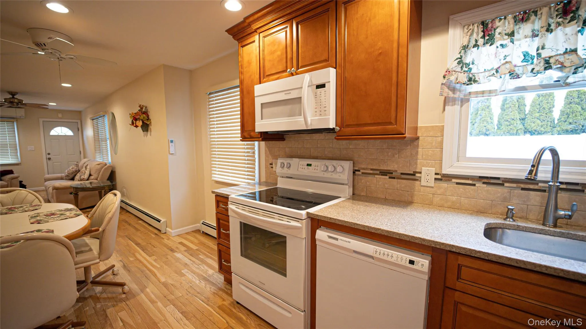 Kitchen with white appliances, brown cabinetry, light stone counters, light wood-style flooring, and recessed lighting Kitchen with white appliances, brown cabinetry, light stone counters, light wood-style flooring, and recessed lighting