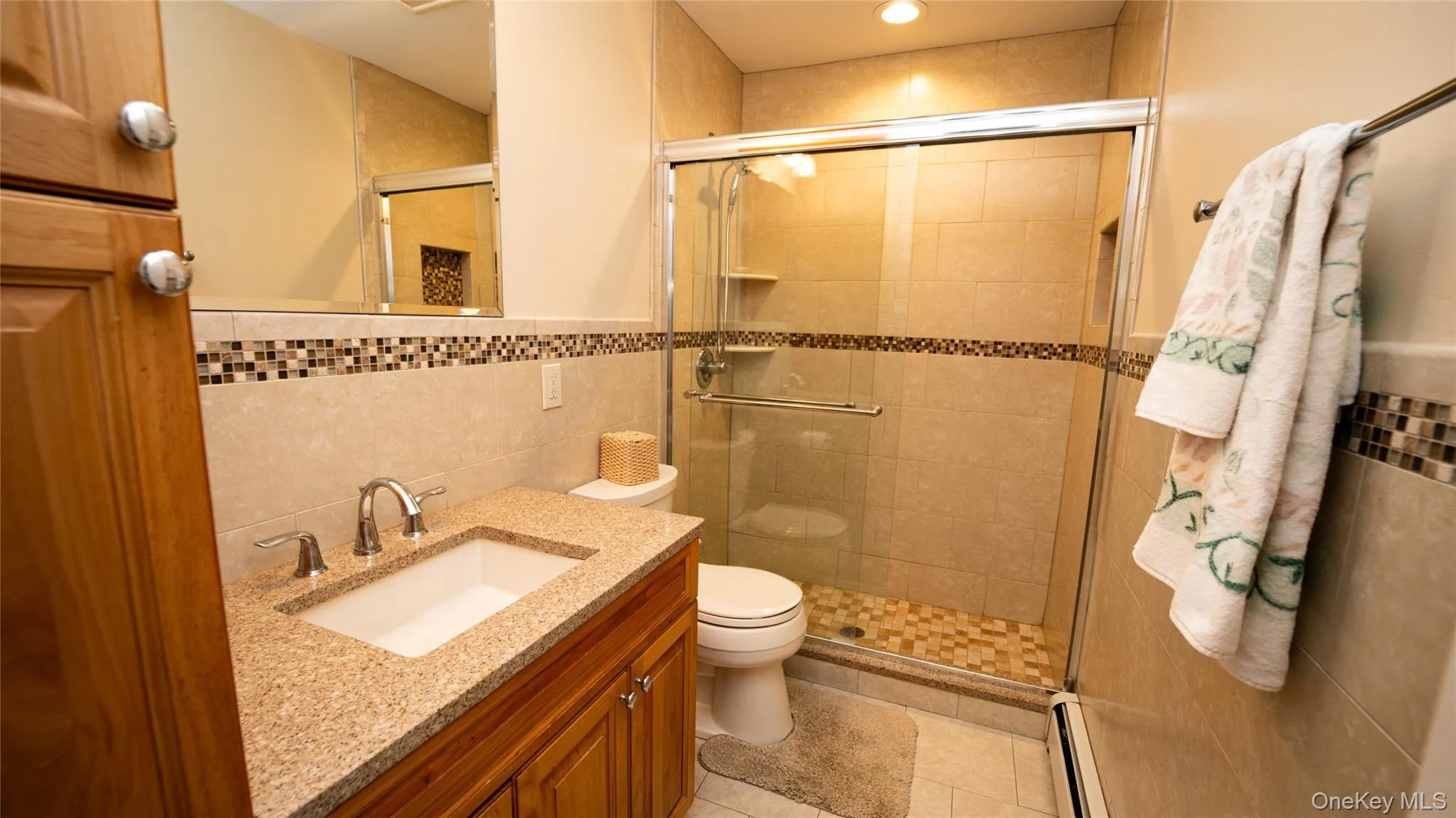 Bathroom with tile walls, vanity, a shower stall, a baseboard heating unit, and light tile patterned flooring Bathroom with tile walls, vanity, a shower stall, a baseboard heating unit, and light tile patterned flooring