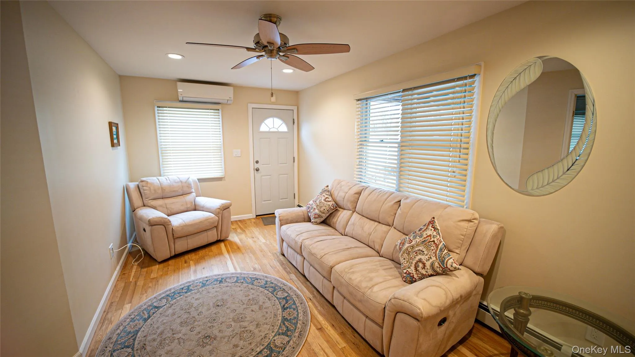 Living area featuring light wood-type flooring, recessed lighting, a ceiling fan, a wall unit AC, and baseboard heating Living area featuring light wood-type flooring, recessed lighting, a ceiling fan, a wall unit AC, and baseboard heating