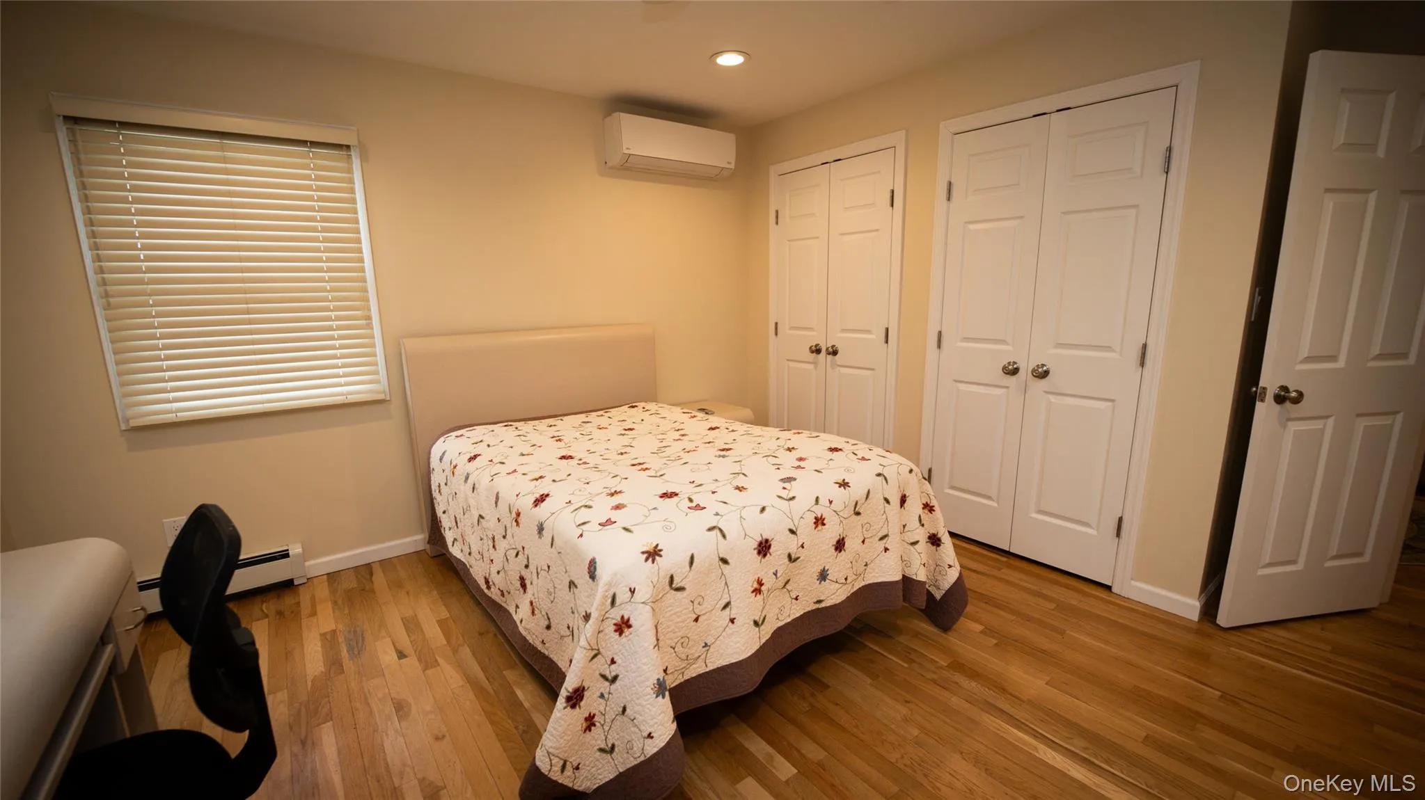 Bedroom featuring multiple closets, wood finished floors, a wall mounted air conditioner, baseboard heating, and recessed lighting Bedroom featuring multiple closets, wood finished floors, a wall mounted air conditioner, baseboard heating, and recessed lighting