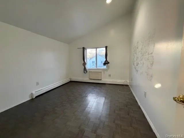 Unfurnished room featuring vaulted ceiling and a baseboard radiator Unfurnished room featuring vaulted ceiling and a baseboard radiator