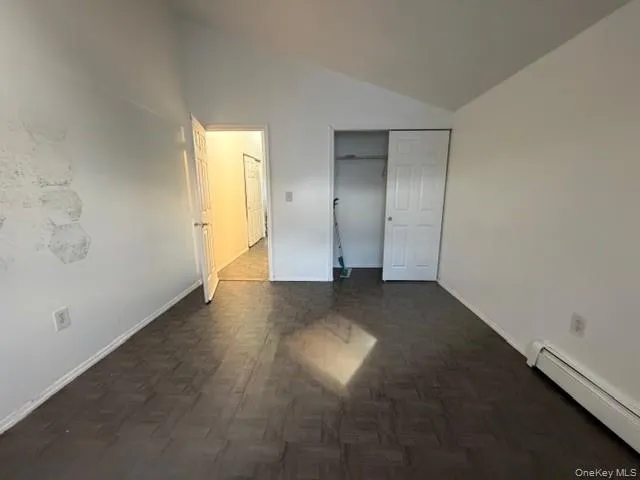 Unfurnished bedroom featuring lofted ceiling, baseboard heating, and a closet Unfurnished bedroom featuring lofted ceiling, baseboard heating, and a closet