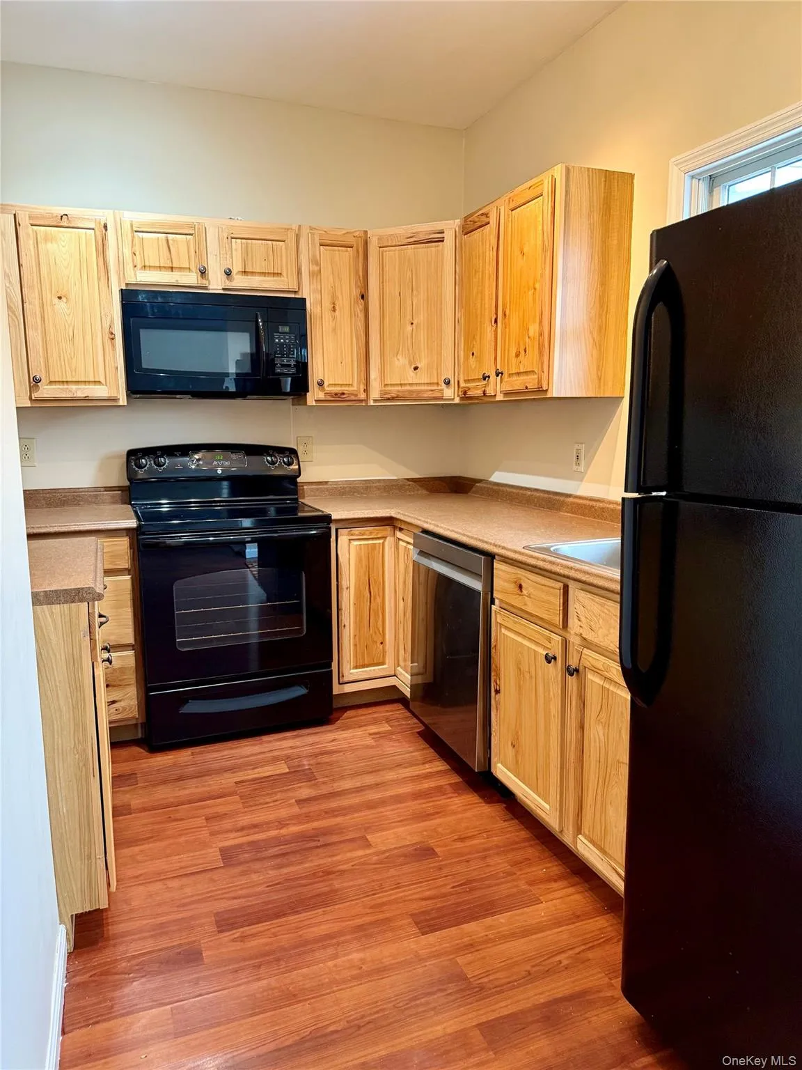 Kitchen featuring black appliances, light brown cabinetry, light wood-style flooring, and light countertops Kitchen featuring black appliances, light brown cabinetry, light wood-style flooring, and light countertops