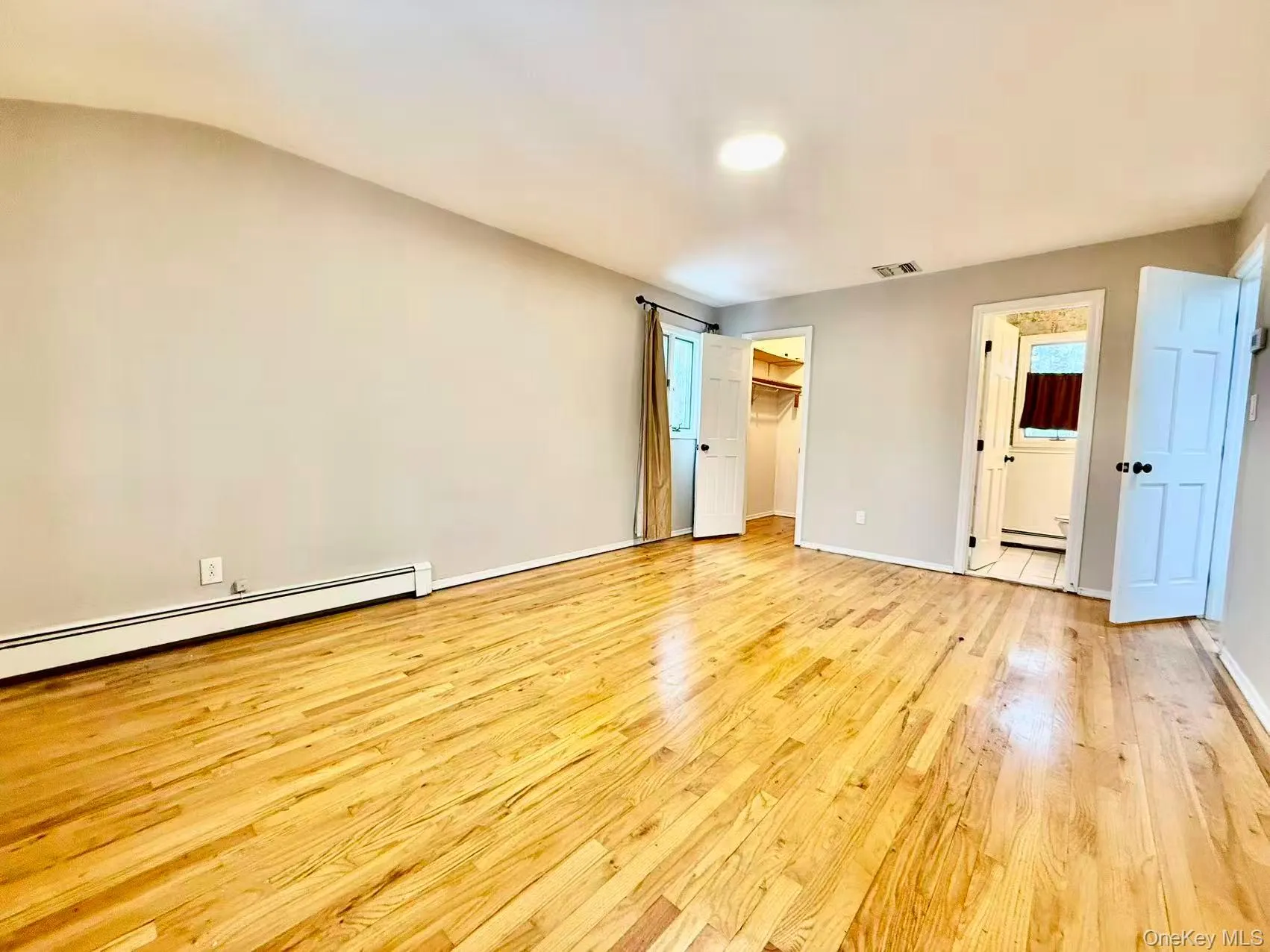 Unfurnished bedroom featuring a spacious closet, light wood-type flooring, a baseboard heating unit, and ensuite bath Unfurnished bedroom featuring a spacious closet, light wood-type flooring, a baseboard heating unit, and ensuite bath
