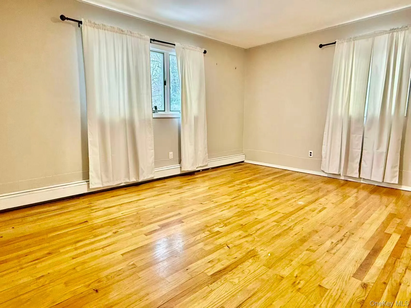 Empty room with light wood finished floors and a baseboard heating unit Empty room with light wood finished floors and a baseboard heating unit