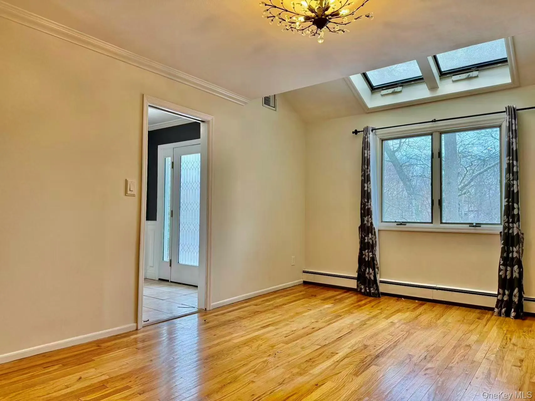 Spare room with light wood-style flooring, a skylight, baseboard heating, crown molding, and vaulted ceiling Spare room with light wood-style flooring, a skylight, baseboard heating, crown molding, and vaulted ceiling
