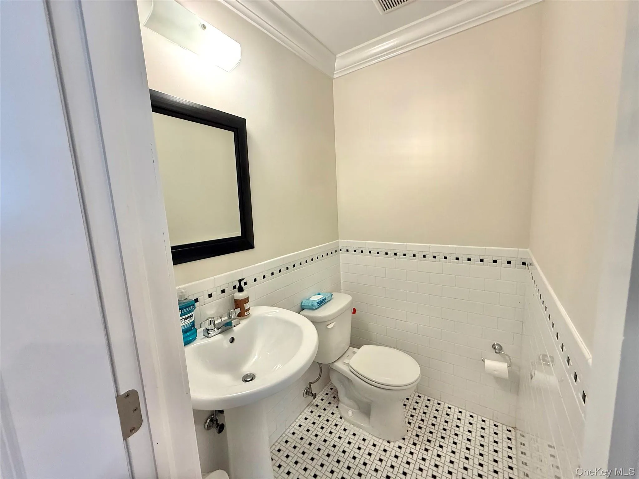 Half bath with ornamental molding, wainscoting, tile patterned flooring, and tile walls Half bath with ornamental molding, wainscoting, tile patterned flooring, and tile walls