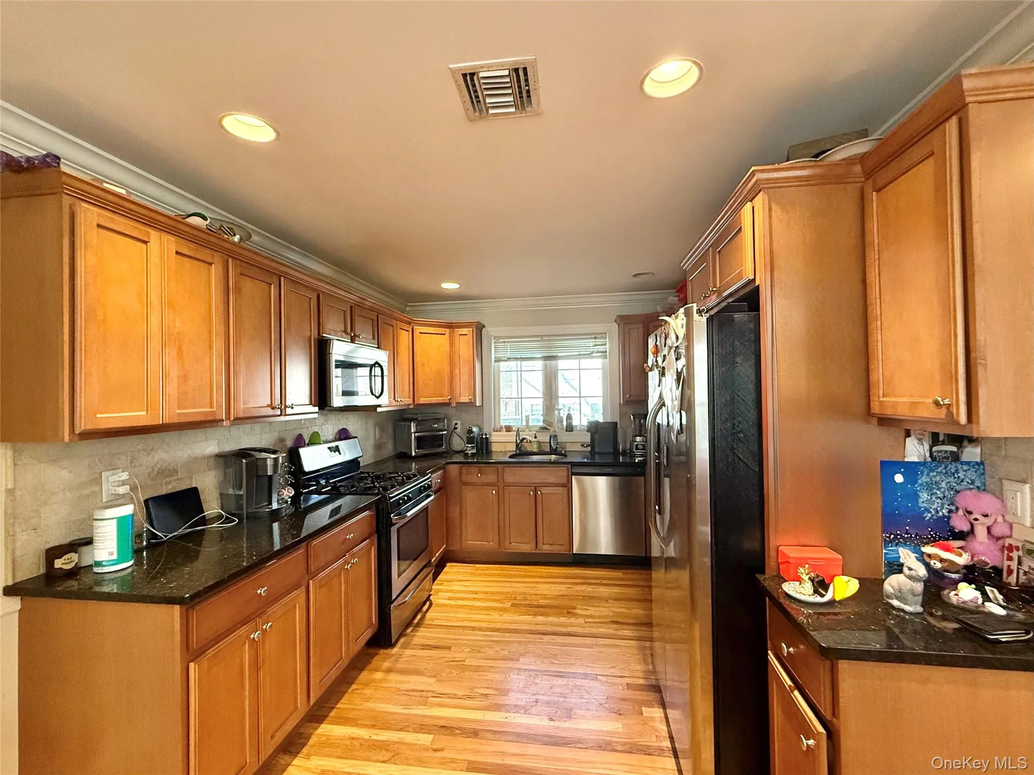 Kitchen featuring brown cabinetry, appliances with stainless steel finishes, dark stone counters, light wood-type flooring, and recessed lighting Kitchen featuring brown cabinetry, appliances with stainless steel finishes, dark stone counters, light wood-type flooring, and recessed lighting