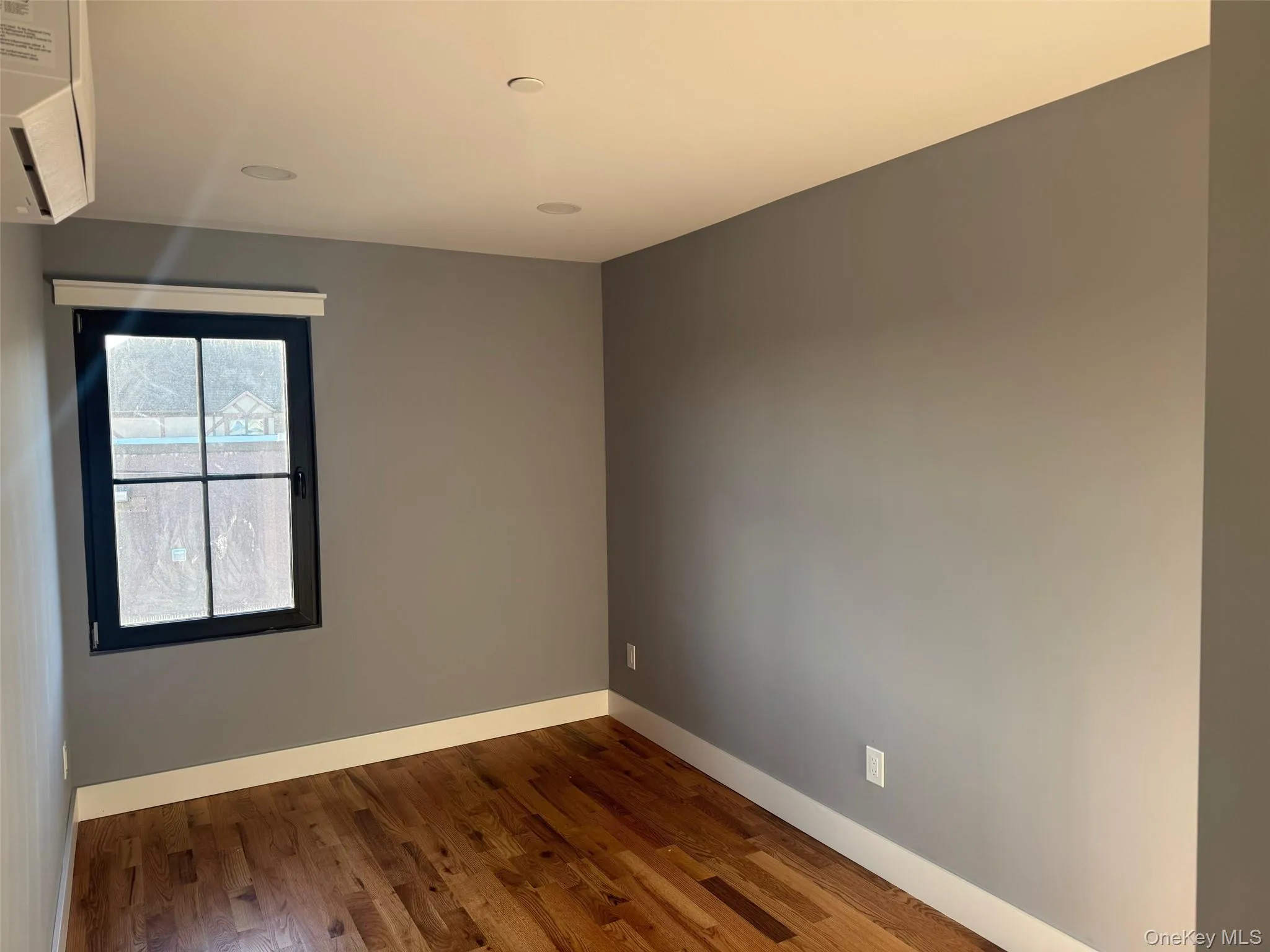 Empty room with wood finished floors and an AC wall unit Empty room with wood finished floors and an AC wall unit