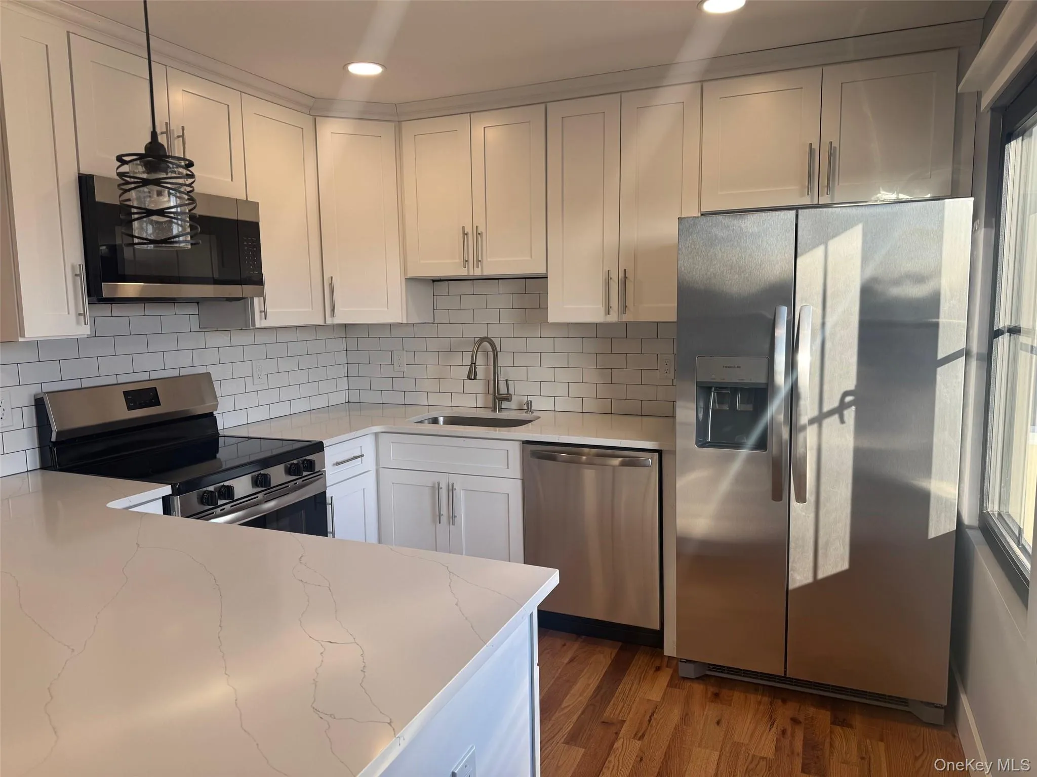 Kitchen featuring appliances with stainless steel finishes, hanging light fixtures, decorative backsplash, white cabinetry, and dark wood-type flooring Kitchen featuring appliances with stainless steel finishes, hanging light fixtures, decorative backsplash, white cabinetry, and dark wood-type flooring
