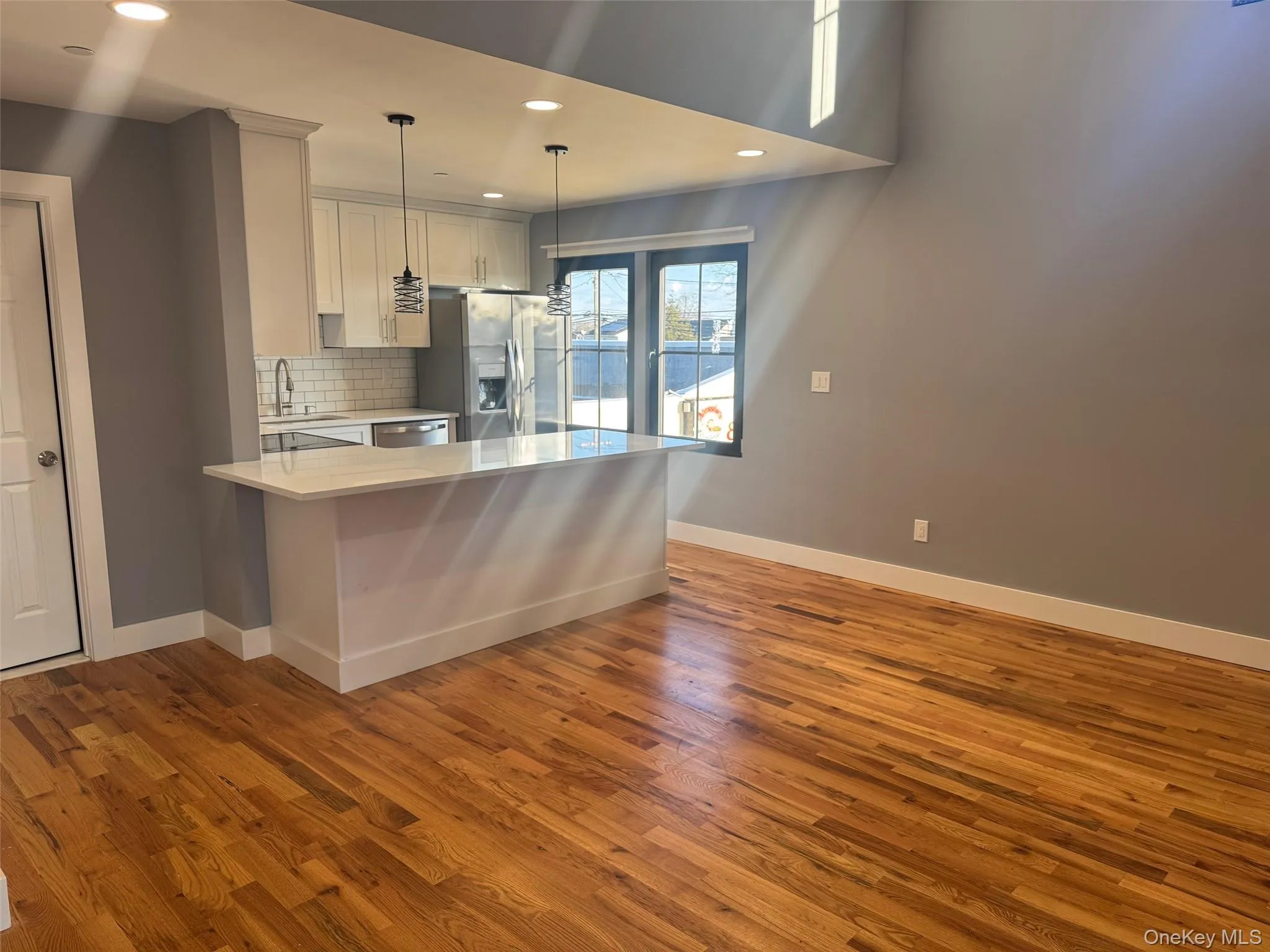 Kitchen with a peninsula, recessed lighting, dark wood finished floors, backsplash, and white cabinets Kitchen with a peninsula, recessed lighting, dark wood finished floors, backsplash, and white cabinets