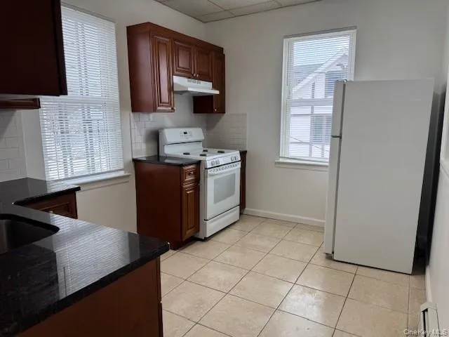 Kitchen with white appliances, decorative backsplash, a paneled ceiling, healthy amount of natural light, and under cabinet range hood Kitchen with white appliances, decorative backsplash, a paneled ceiling, healthy amount of natural light, and under cabinet range hood