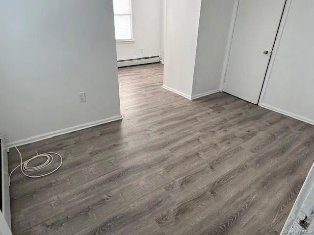 Unfurnished bedroom with wood finished floors and a baseboard heating unit Unfurnished bedroom with wood finished floors and a baseboard heating unit