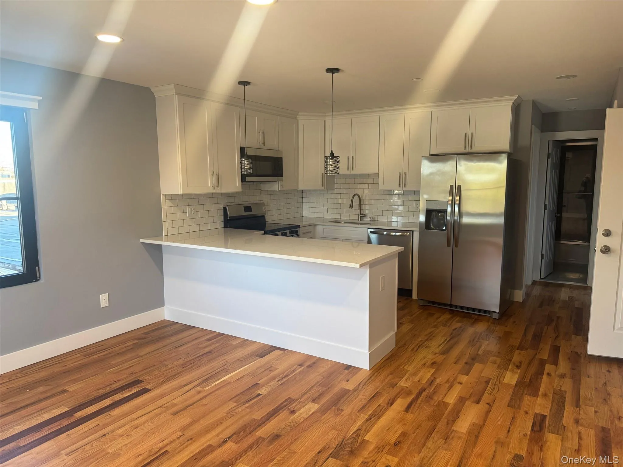 Kitchen featuring stainless steel appliances, a peninsula, decorative backsplash, decorative light fixtures, and dark wood-style flooring Kitchen featuring stainless steel appliances, a peninsula, decorative backsplash, decorative light fixtures, and dark wood-style flooring