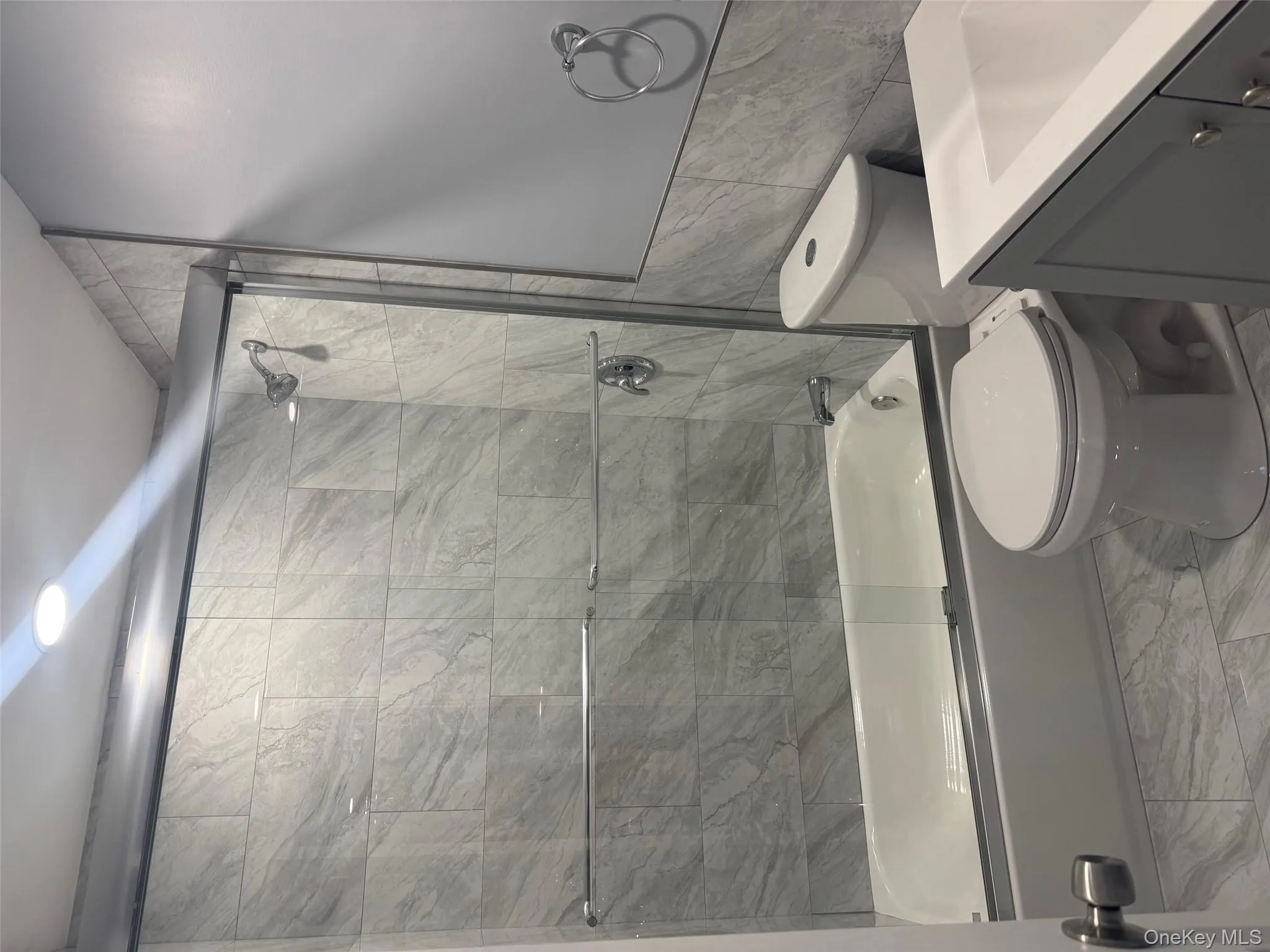 Full bathroom with tile walls, shower / bath combination with glass door, vanity, and marble look tile flooring Full bathroom with tile walls, shower / bath combination with glass door, vanity, and marble look tile flooring