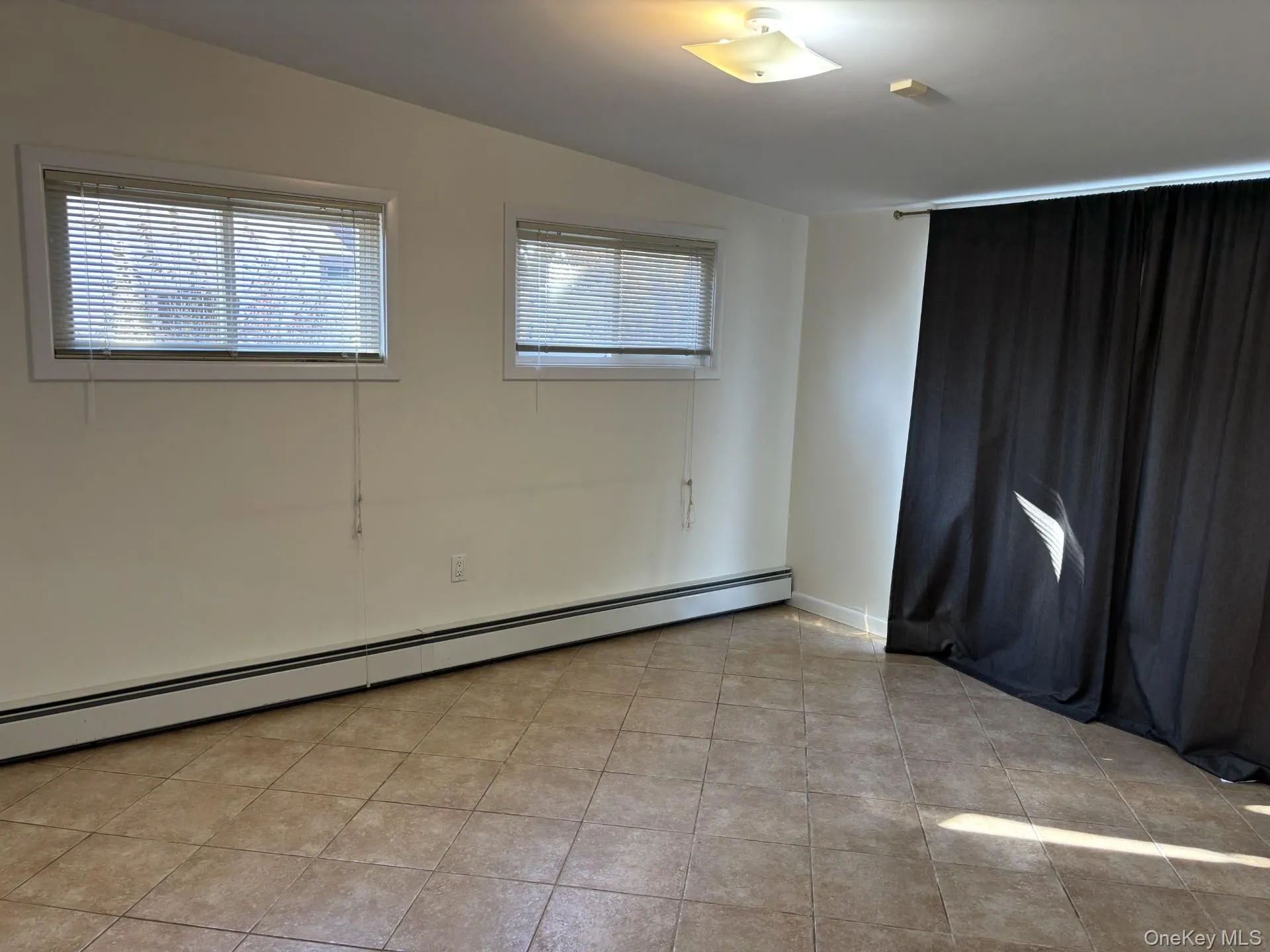 Empty room featuring baseboard heating, lofted ceiling, and light tile patterned floors Empty room featuring baseboard heating, lofted ceiling, and light tile patterned floors