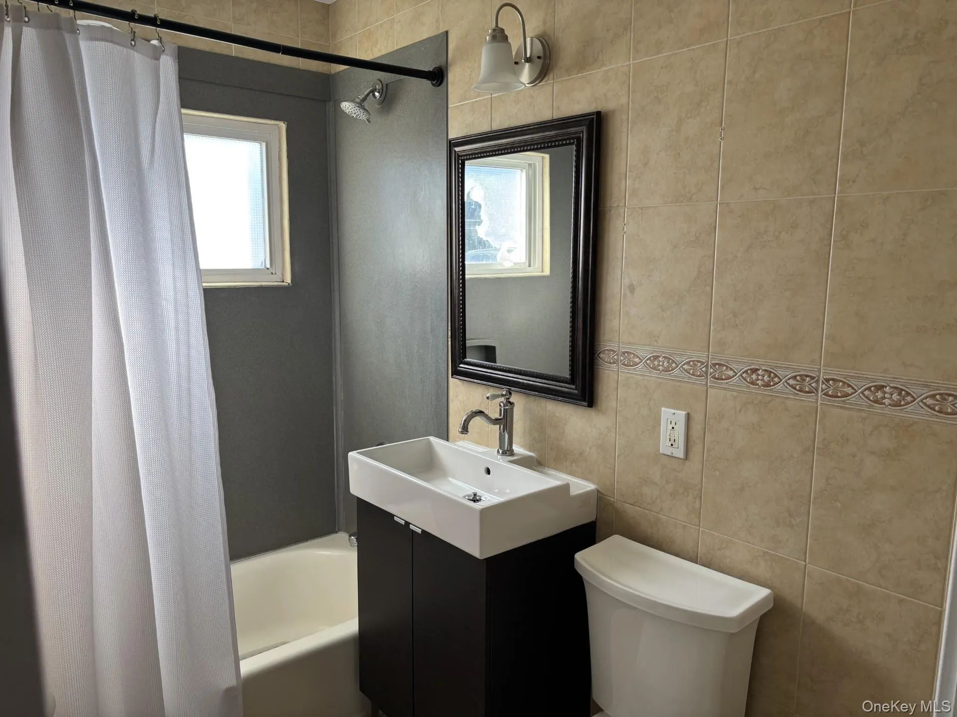 Full bath with shower / bathtub combination with curtain, vanity, tile walls, and healthy amount of natural light Full bath with shower / bathtub combination with curtain, vanity, tile walls, and healthy amount of natural light