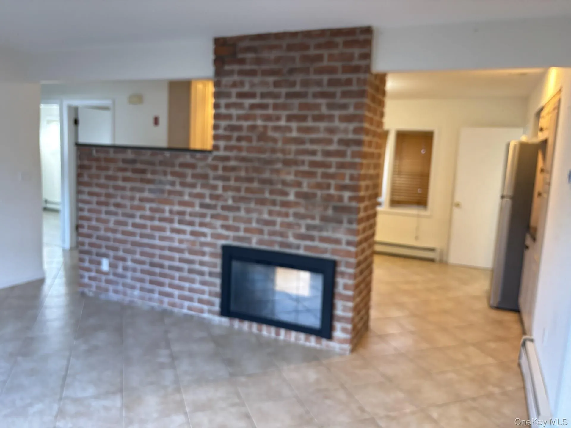 Unfurnished living room with a brick fireplace, a baseboard radiator, and light tile patterned floors Unfurnished living room with a brick fireplace, a baseboard radiator, and light tile patterned floors