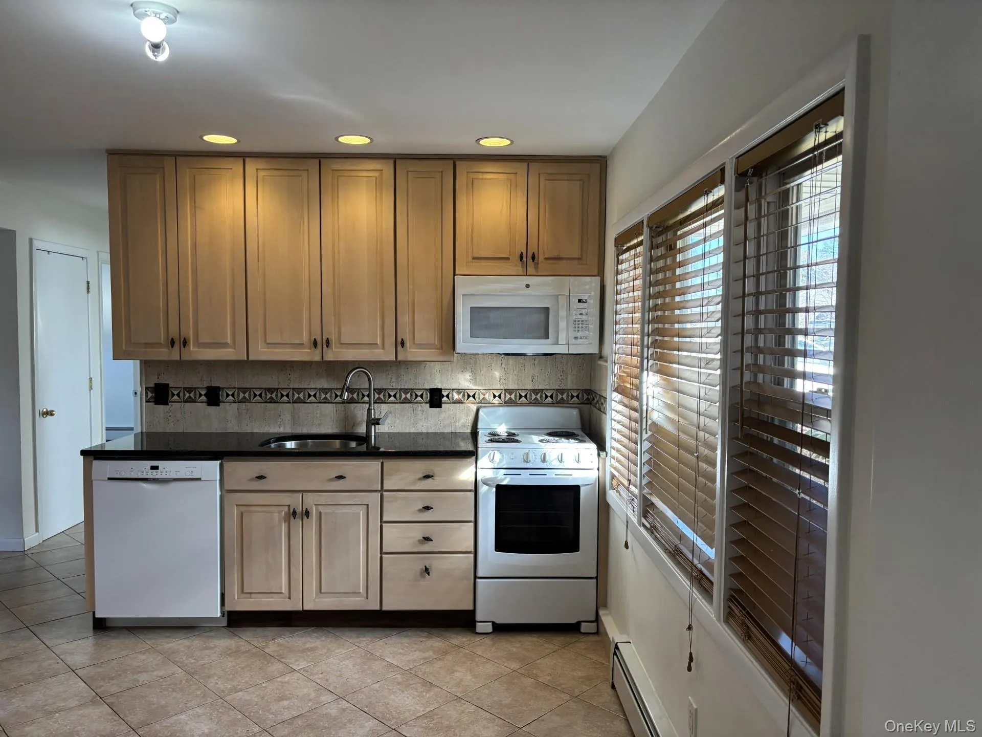 Kitchen featuring white appliances, backsplash, dark stone counters, light tile patterned floors, and recessed lighting Kitchen featuring white appliances, backsplash, dark stone counters, light tile patterned floors, and recessed lighting