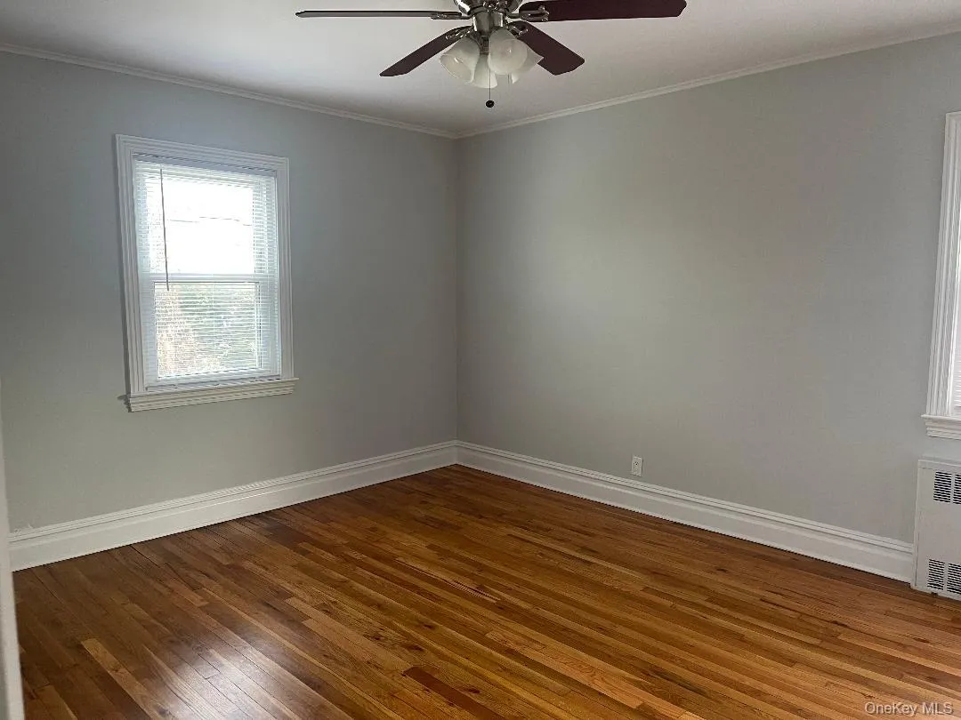 Empty room with crown molding, dark wood finished floors, radiator, and a ceiling fan Empty room with crown molding, dark wood finished floors, radiator, and a ceiling fan