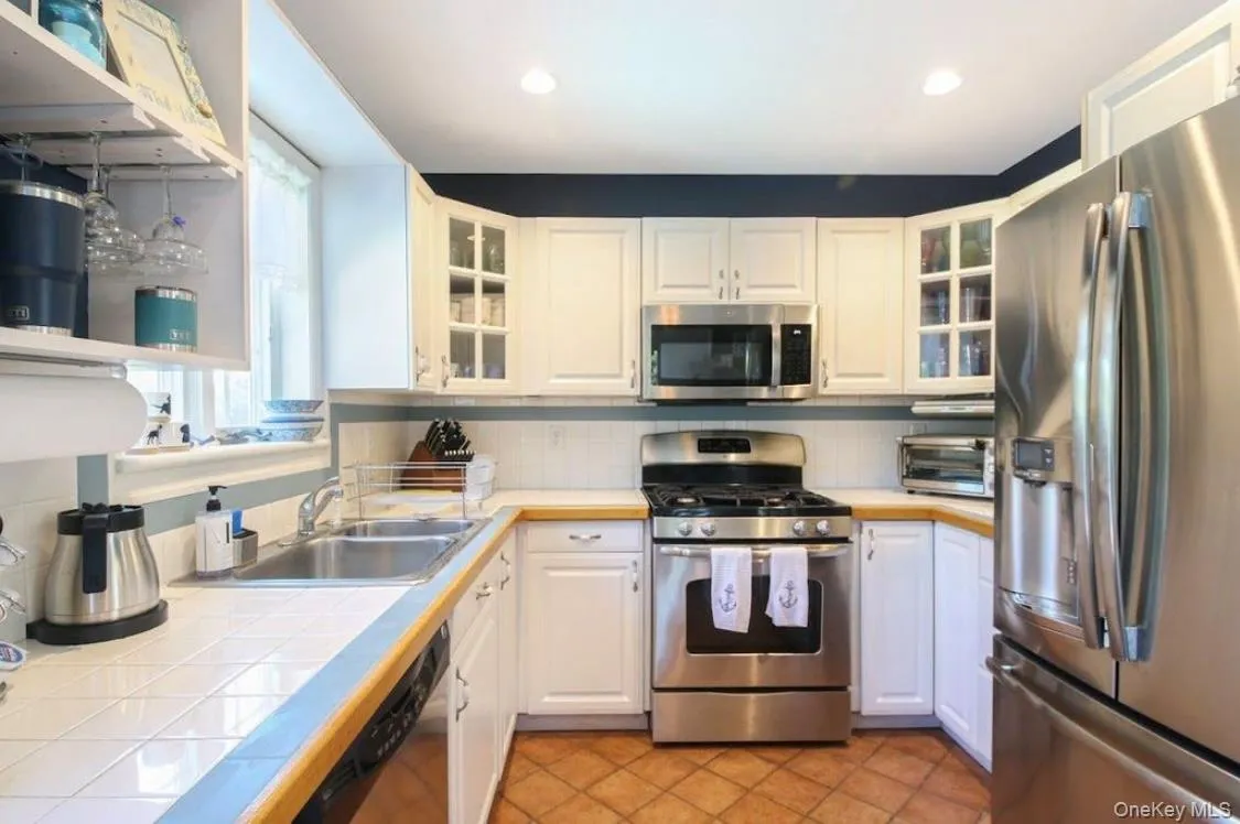 Kitchen featuring appliances with stainless steel finishes, white cabinets, glass insert cabinets, backsplash, and recessed lighting Kitchen featuring appliances with stainless steel finishes, white cabinets, glass insert cabinets, backsplash, and recessed lighting