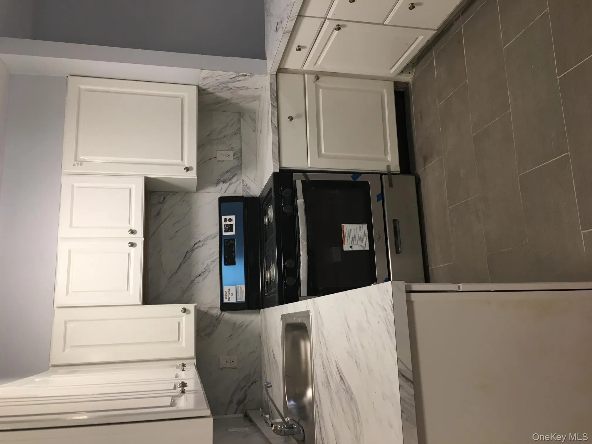 Kitchen with light countertops, white cabinetry, black range, dark tile patterned floors, and tasteful backsplash Kitchen with light countertops, white cabinetry, black range, dark tile patterned floors, and tasteful backsplash