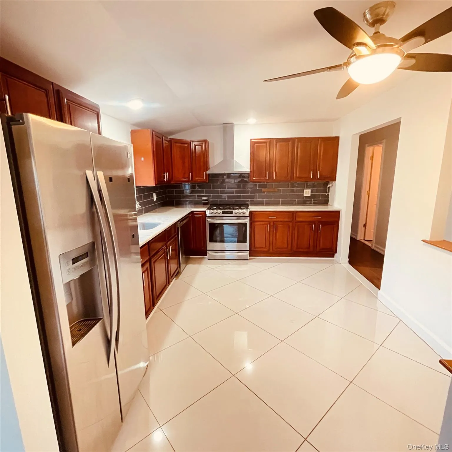 Kitchen featuring stainless steel appliances, wall chimney exhaust hood, ceiling fan, lofted ceiling, and tasteful backsplash Kitchen featuring stainless steel appliances, wall chimney exhaust hood, ceiling fan, lofted ceiling, and tasteful backsplash