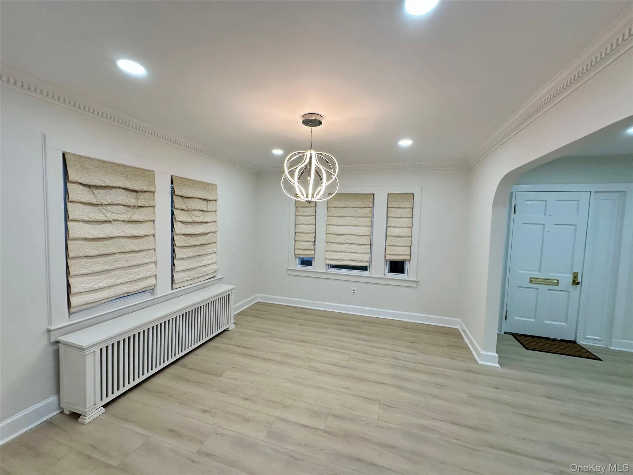 Unfurnished dining area with radiator heating unit, arched walkways, light wood-style floors, recessed lighting, and a chandelier Unfurnished dining area with radiator heating unit, arched walkways, light wood-style floors, recessed lighting, and a chandelier