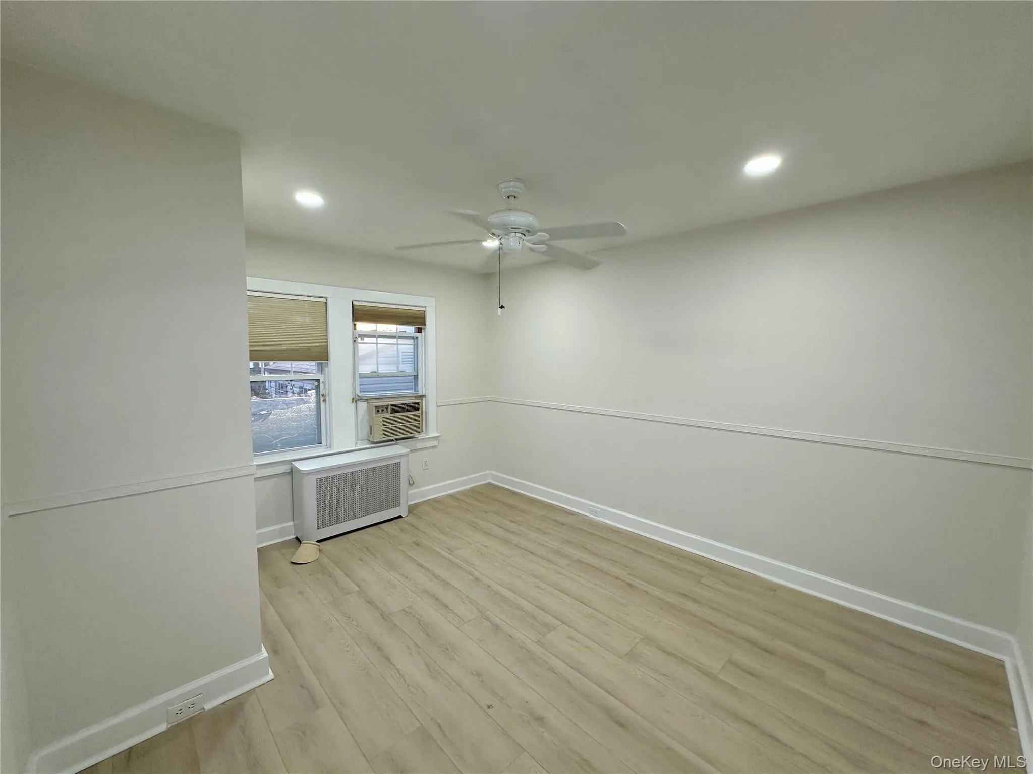 Unfurnished room with light wood-style floors, recessed lighting, radiator heating unit, ceiling fan, and cooling unit Unfurnished room with light wood-style floors, recessed lighting, radiator heating unit, ceiling fan, and cooling unit