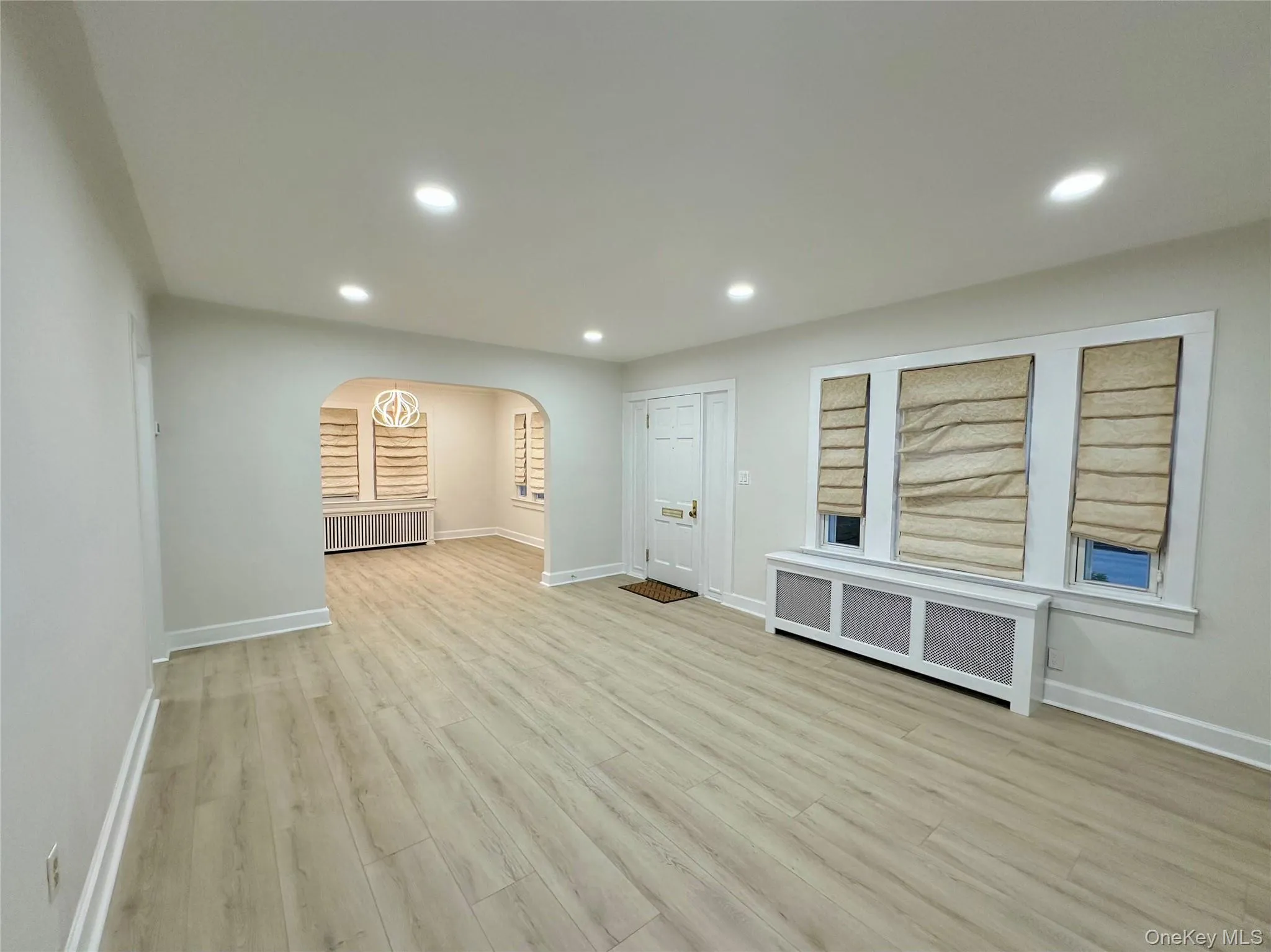 Empty room featuring radiator, arched walkways, light wood finished floors, and recessed lighting Empty room featuring radiator, arched walkways, light wood finished floors, and recessed lighting
