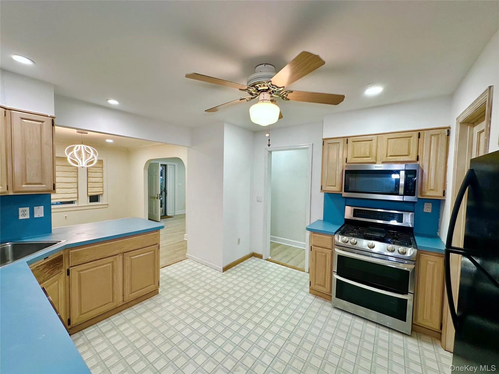 Kitchen with appliances with stainless steel finishes, arched walkways, light brown cabinets, recessed lighting, and light floors Kitchen with appliances with stainless steel finishes, arched walkways, light brown cabinets, recessed lighting, and light floors
