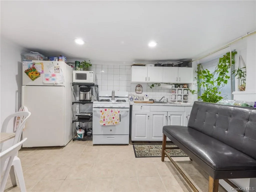 Kitchen with white appliances, light countertops, white cabinets, decorative backsplash, and light tile patterned floors Kitchen with white appliances, light countertops, white cabinets, decorative backsplash, and light tile patterned floors