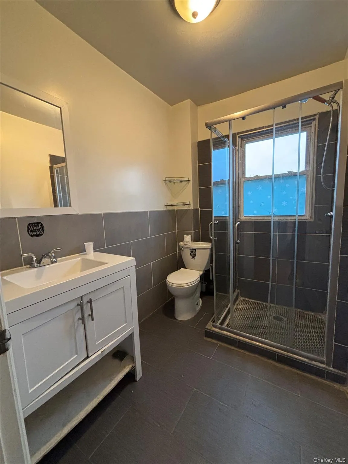 Full bathroom with tile walls, vanity, a stall shower, dark tile patterned floors, and a wainscoted wall Full bathroom with tile walls, vanity, a stall shower, dark tile patterned floors, and a wainscoted wall