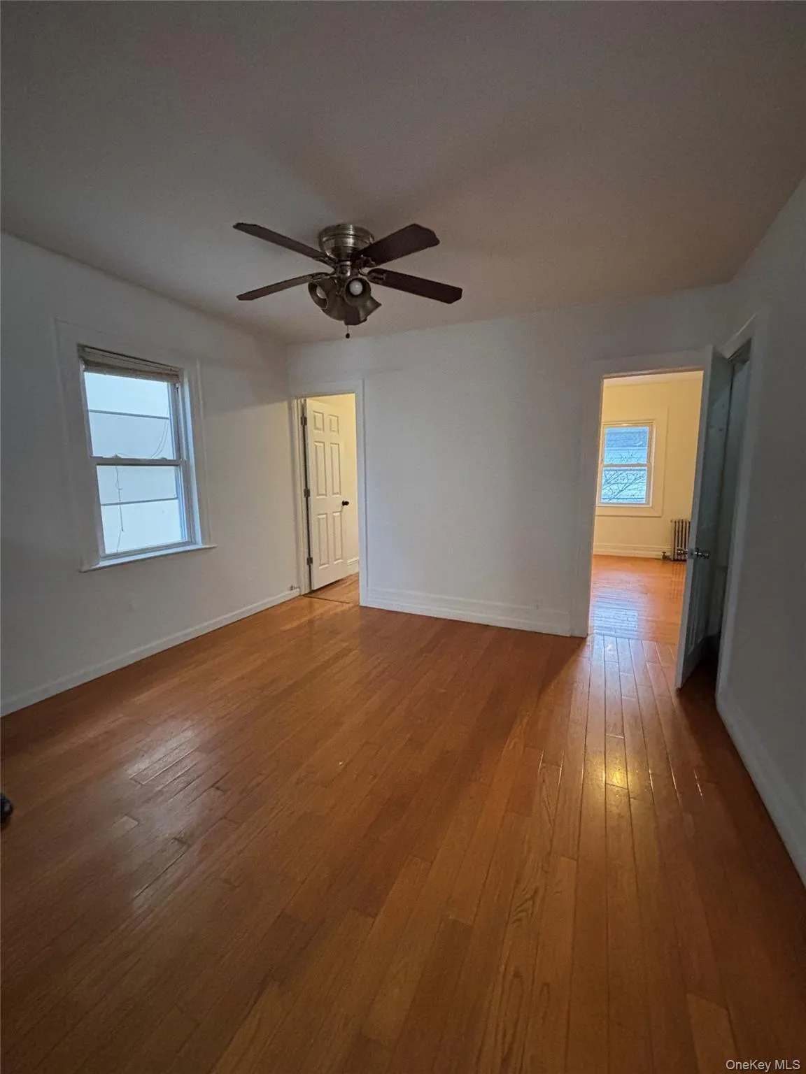 Unfurnished room featuring healthy amount of natural light, light wood-style flooring, a ceiling fan, and radiator heating unit Unfurnished room featuring healthy amount of natural light, light wood-style flooring, a ceiling fan, and radiator heating unit
