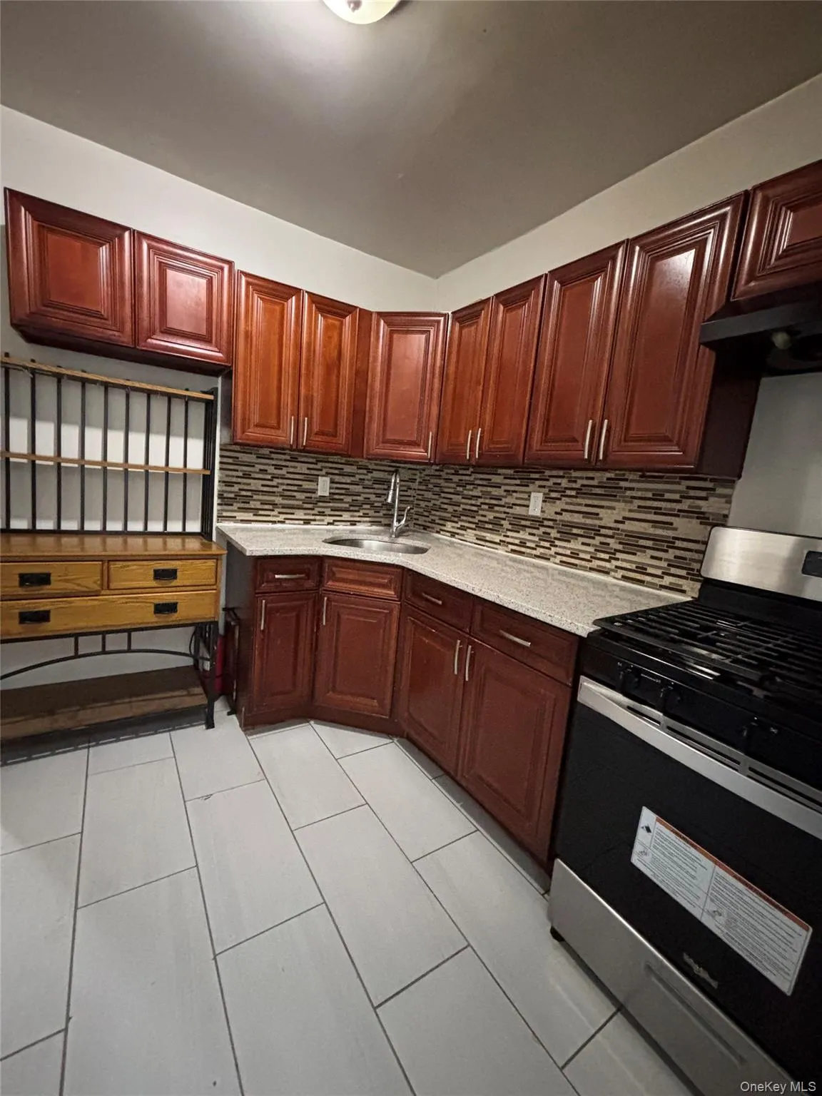 Kitchen with stainless steel range with gas stovetop, decorative backsplash, light stone counters, exhaust hood, and reddish brown cabinets Kitchen with stainless steel range with gas stovetop, decorative backsplash, light stone counters, exhaust hood, and reddish brown cabinets